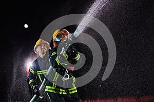 Firefighters using a water hose to eliminate a fire hazard. Team of female and male firemen in dangerous rescue mission