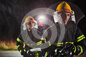 Firefighters using a water hose to eliminate a fire hazard. Team of female and male firemen in dangerous rescue mission