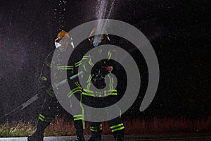 Firefighters using a water hose to eliminate a fire hazard. Team of female and male firemen in dangerous rescue mission