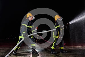 Firefighters using a water hose to eliminate a fire hazard. Team of female and male firemen in dangerous rescue mission