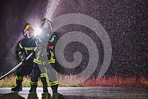 Firefighters using a water hose to eliminate a fire hazard. Team of female and male firemen in dangerous rescue mission