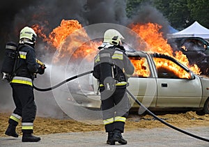 Firefighters at work next to a burning car