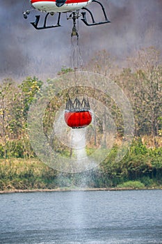 Firefighting helicopter refills water bucket in a pond