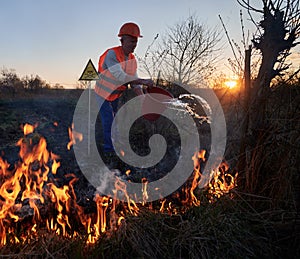 Fireman ecologist fighting fire in field in the evening