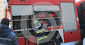 Fireman folds the hose into the fire engine truck. View from the back, unrecognizable in helmet and uniform. Equipment