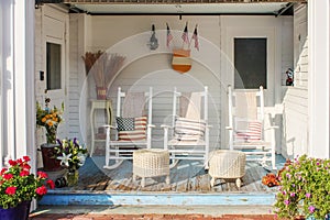 Fireman and patriotic themed worn wooden front porch in Cape Cod with three white rocking chairs and pillows and wicker foot