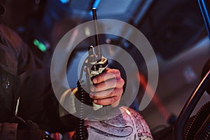 Fireman in a protective uniform sitting in the fire truck and holding walkie-talkie. Hand close up.