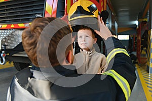 A fireman shows his work to his young son. A boy in a firefighter& x27;s helmet