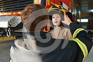 A fireman shows his work to his young son. A boy in a firefighter& x27;s helmet