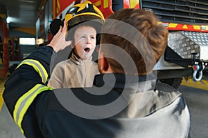 A fireman shows his work to his young son. A boy in a firefighter& x27;s helmet