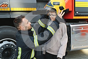 A fireman shows his work to his young son. A boy in a firefighter& x27;s helmet