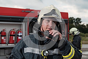 fireman using walkie talkie at rescue action fire truck and fireman& x27;s team in background.