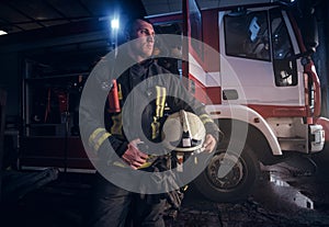 Fireman wearing uniform looking outside while standing near a fire truck in a garage of a fire department
