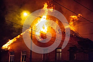 Firemen direct water stream on burning house.building in full flaming inferno, and a firefighter fighting to get control of the fl