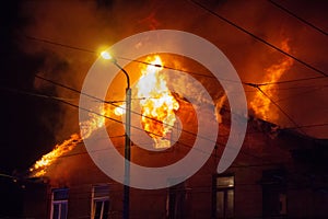 Firemen direct water stream on burning house.building in full flaming inferno, and a firefighter fighting to get control of the fl