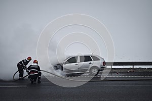 Firemen extinguish a burning car on a highway