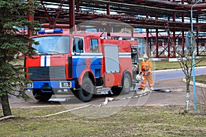 Firemen rescue workers in fireproof suits came to extinguish a fire in a fire truck and stretch the hoses in a large industrial