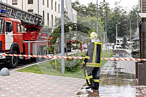 Firemen un uniform standing behind fire tape and many fire engine trucks with ladder at accident in highrise tower