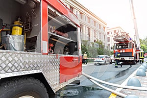 Firemen wearing uniform standing behind fire tape and many fire engine trucks with ladder at accident in highrise tower