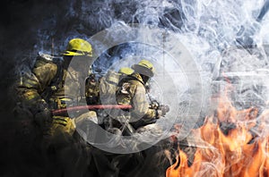 Firemen wearing yellow clothes extinguish fires that are extremely hot. There are both flames and smoke