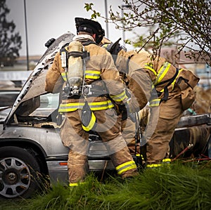 Firemen working at scene of burned car wearing protective clothing and gear