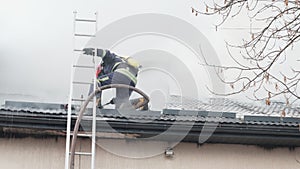 Firemen working with tools and hose on burnt-out roof.