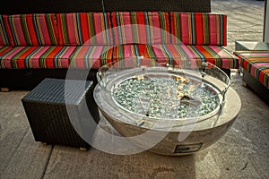 Firepit with glass pebbles in outdoor seating area with brightly striped and wiker furniture