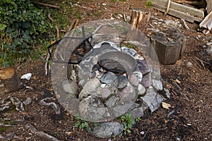 Fireplace with empty brass pot and empty black grill between grey stones and brown forest floor, fireplaces offer hikers a cooking