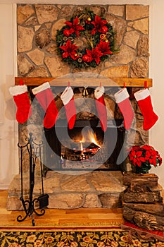 Fireplace with six Christmas stockings, logs, bells and wreath.