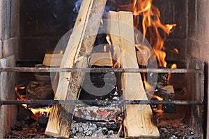 Firewood is burning in fireplace behind metal grate closeup