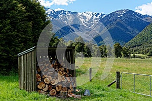 A firewood shed stocked with firewood, snow capped mountains in the background