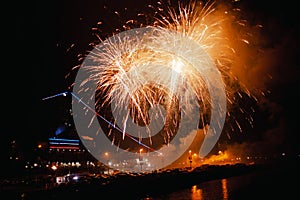 Firework show in the city - orange fireworks above the bay with reflecions in water