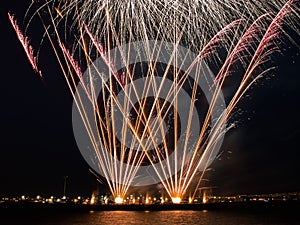 Fireworks burst in the night sky with light trails and clear base of fireworks over the sea