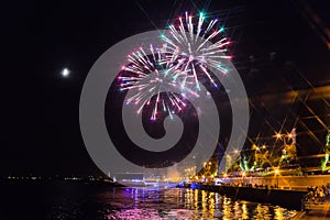 Fireworks over the Volga river in Saratov, Russia. Evening cityscape. People on the street. The moon