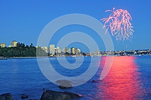 Fireworks shining above city center and reflecting on sea water at blue hour