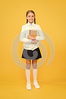 A firm knowledge base for future. Adorable small girl holding book on yellow background. Cute little child with book