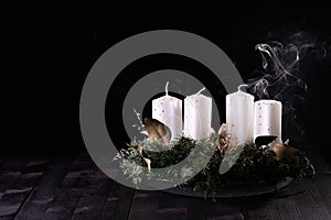 First Advent - Advent wreath from fir and evergreen branches with blown out candle on dark wooden table. White smoke on black