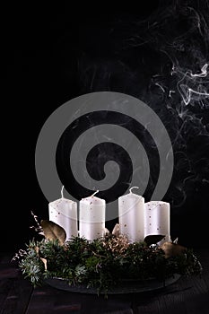 First Advent - Advent wreath from fir and evergreen branches with blown out candle on dark wooden table. White smoke on black