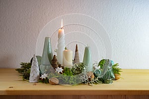 First Advent, decoration with four different candles, one is lit, moss, green glass Christmas balls and cinnamon stars on a wooden