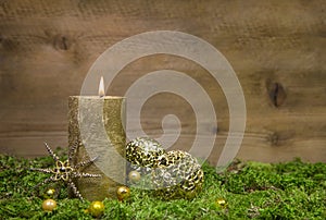 First advent: golden candle burning before wooden background.