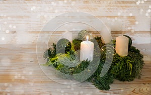 First advent, natural advent wreath with white candles, one is lit, green Christmas baubles made from glass, wooden background