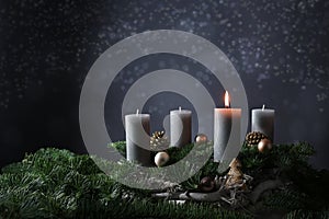 First advent with one burning candle on fir branches with Christmas decoration against a dark grey background, copy space