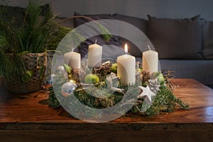 First Advent, wreath with one burning white candle and Christmas decoration on a wooden table in front of the couch, festive home