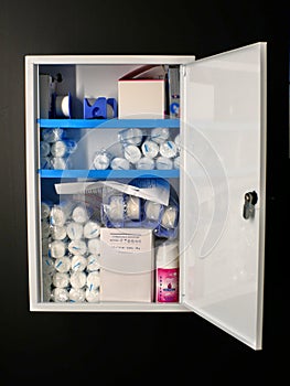 First aid cabinet mounted on a black wall, filled with bandage, antiseptic spray