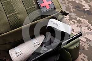 First aid kit with medical tourniquet and elastic bands on military fabric, closeup