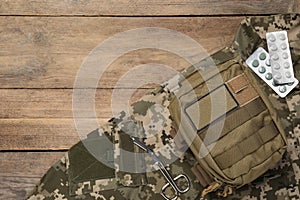 First aid kit and military uniform on wooden table, flat lay. Space for text