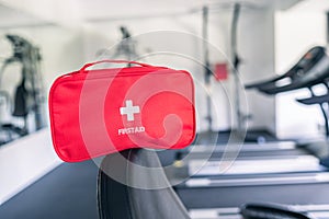 First aid kit red box in the fitness gym opposite the sport equipment and jogging simulators. Healthy lifestyle, safety and help
