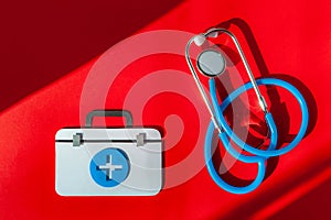 First aid kit with stethoscope on red background.