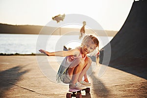 First attempts. Sunny day. Kid have fun with skate at the ramp. Cheerful little girl