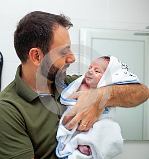 First bath of newborn baby boy. The baby is in the bathrobe in his father`s arms